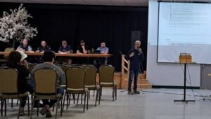 Un homme micro devant une petite audience explique le document projeté sur une toile