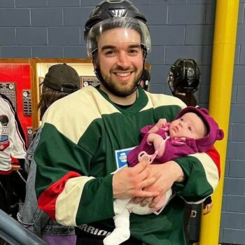 Un papa de famille en uniforme de joueur de hockey tenant un bébé dans ses bras