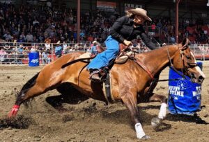 Femme sur une cheval à toute vitesse contournant un baril bleu devant une foule de spectateur