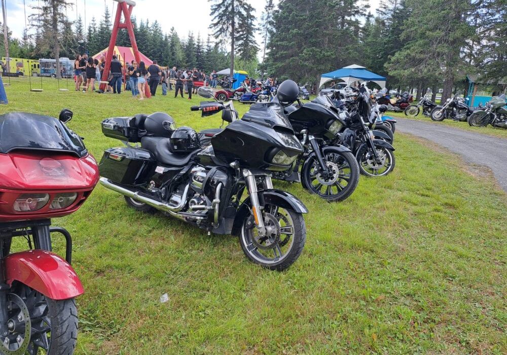 Plusieurs motos de marque populaire devant des festivaliers regroupés ensemble durant un festival de moto lors d'une journée chaude et nuageuse