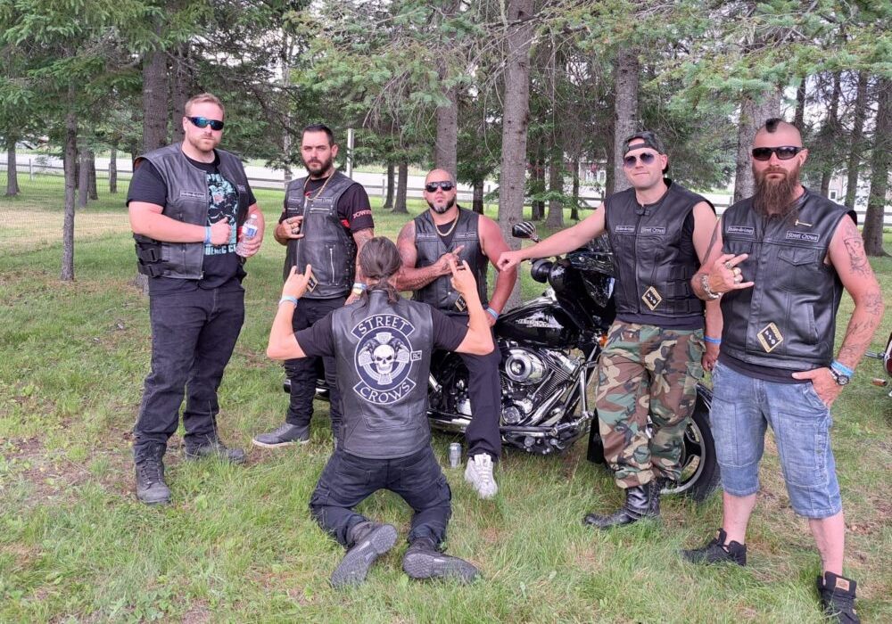 Photo d'un club de moto affichant fièrement leur identité de motard, devant plusieurs arbres et lors d'une journée ensoleillée