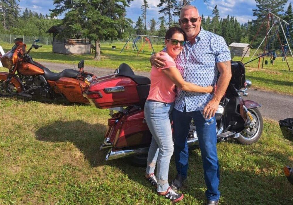 Un couple se donne l'accolade devant leur moto lors d'une journée ensoleillée