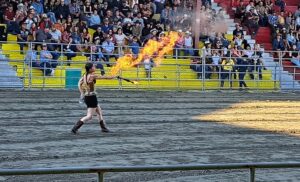 Une femme costumé crache du feu pour divertir la foule lors d'un rodéo
