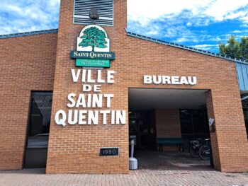 Édifice municipale en briques indiqué en lettre Ville de Saint-Quentin avec le logo de la Ville en haut des lettres. en haut de l'édifice il y a un ciel bleu avec des nuages