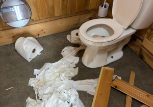 Papier de toilette étendu sur le sol d'une salle de bain publique. Plusieurs morceaux de bois cassé traîne au sol.