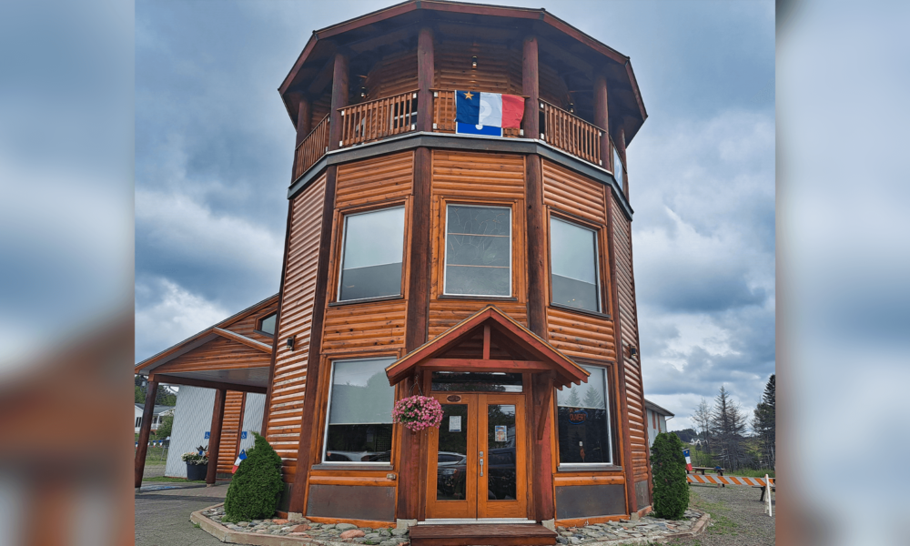 Tour des Pionniers en bois brun affichant un drapeau de l'Acadie en hauteur, lors d'une pluvieuse et nuageuse