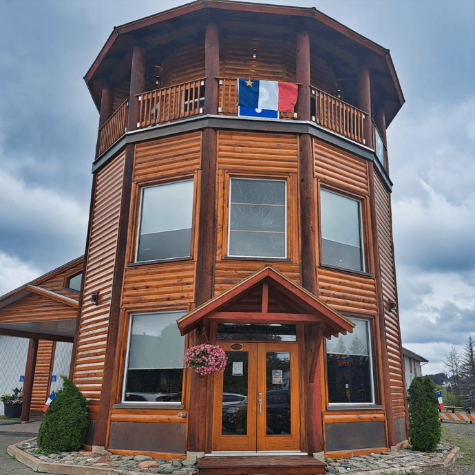 Tour des Pionniers en bois brun affichant un drapeau de l'Acadie en hauteur, lors d'une pluvieuse et nuageuse