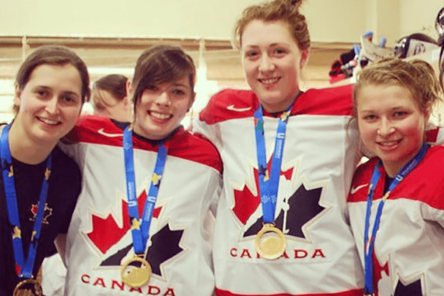 Quatre joueuses de hockey portant fièrement chacune leur médaille d'or dans l'uniforme du Canada.