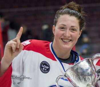 Une joueuse de hockey en uniforme blanc et rouge, tout sourire tenant une coupe de championnat