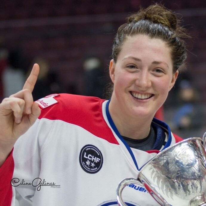 Une joueuse de hockey en uniforme blanc et rouge, tout sourire tenant une coupe de championnat