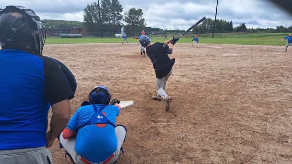 Lors d'un match de softball, un batteur pourtant un chandail noir s'élance.