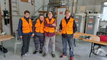 Quatre bénévoles vêtus de vestes orange, prêts à faire l'enregistrement des orignaux abattus.