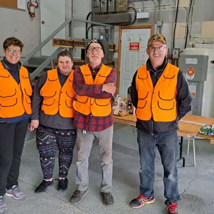 Quatre bénévoles vêtus de vestes orange, prêts à faire l'enregistrement des orignaux abattus.