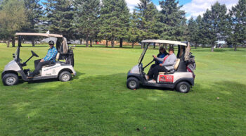 Trois personnes pour deux voiturettes de golf tout sourire lors d'une journée ensoleillée.
