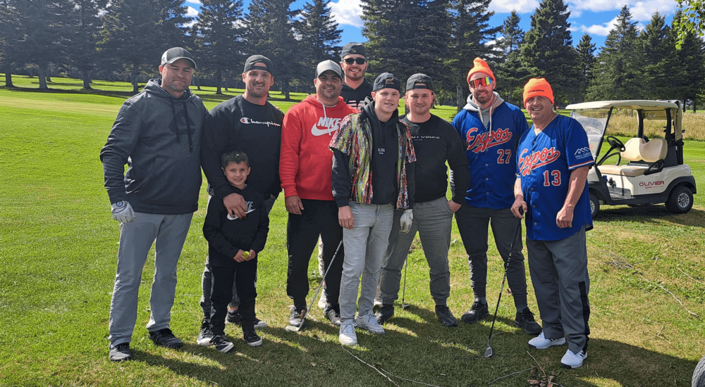 8 joueurs de golf et un enfant se tiennent debout tout sourire pour une photo pendant un tournoi de golf lors d'une journée ensoleillée.