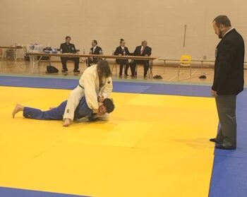 Deux Judokas combattent lors d'une compétition de Judo. l'homme en blanc domine son adversaire en bleu.