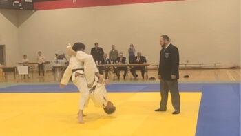 Combat de judo, un judoka tient son adversaire dans les airs la tête à l'envers.