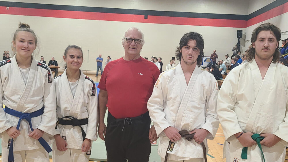 4 judokas avec au milieu un homme au gilet rouge, lors d'une compétition de Judo à l'intérieur d'un gymnase.