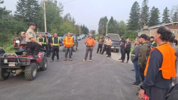 Un garde forestier debout sur un VTT fait un discours à des citoyens placés en rond.