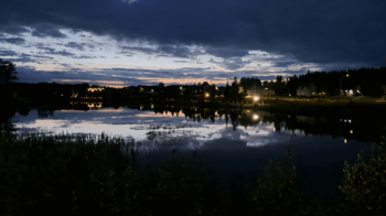 Lac et arbuste en plein soirée avec une ciel nuageux et avec un éclairage qui reflète sur le lac.