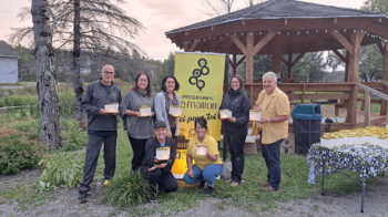 Sept personnes devant une affiche jaune indiquant le programme Le Maillon, en tenant chacune une lanterne lumineuse en début de soirée.