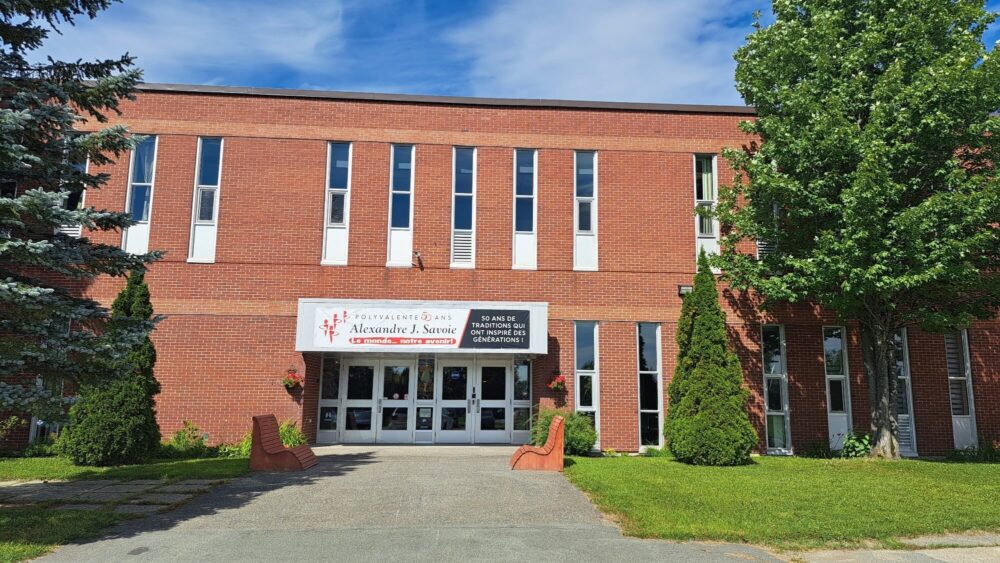 École en briques rouges avec une pelouse verte devant et quelques arbres lors d'une journée ensoleillée.