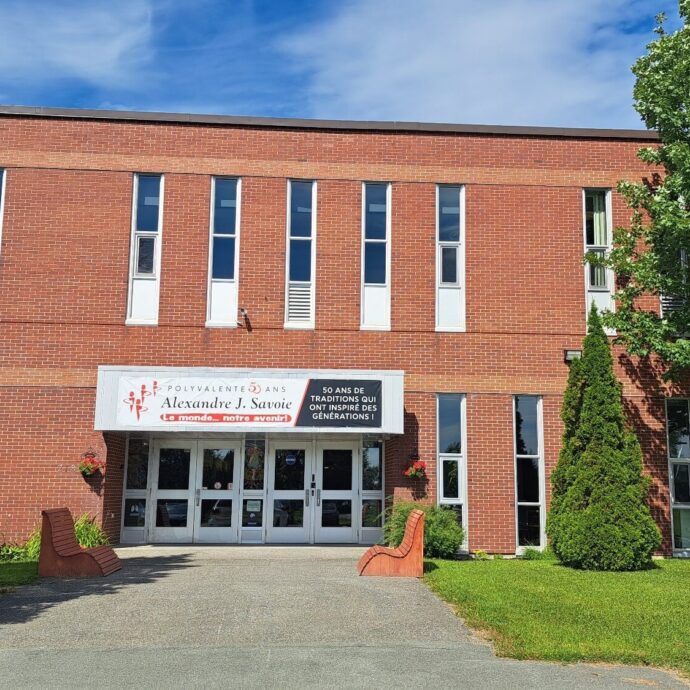 École en briques rouges avec une pelouse verte devant et quelques arbres lors d'une journée ensoleillée.