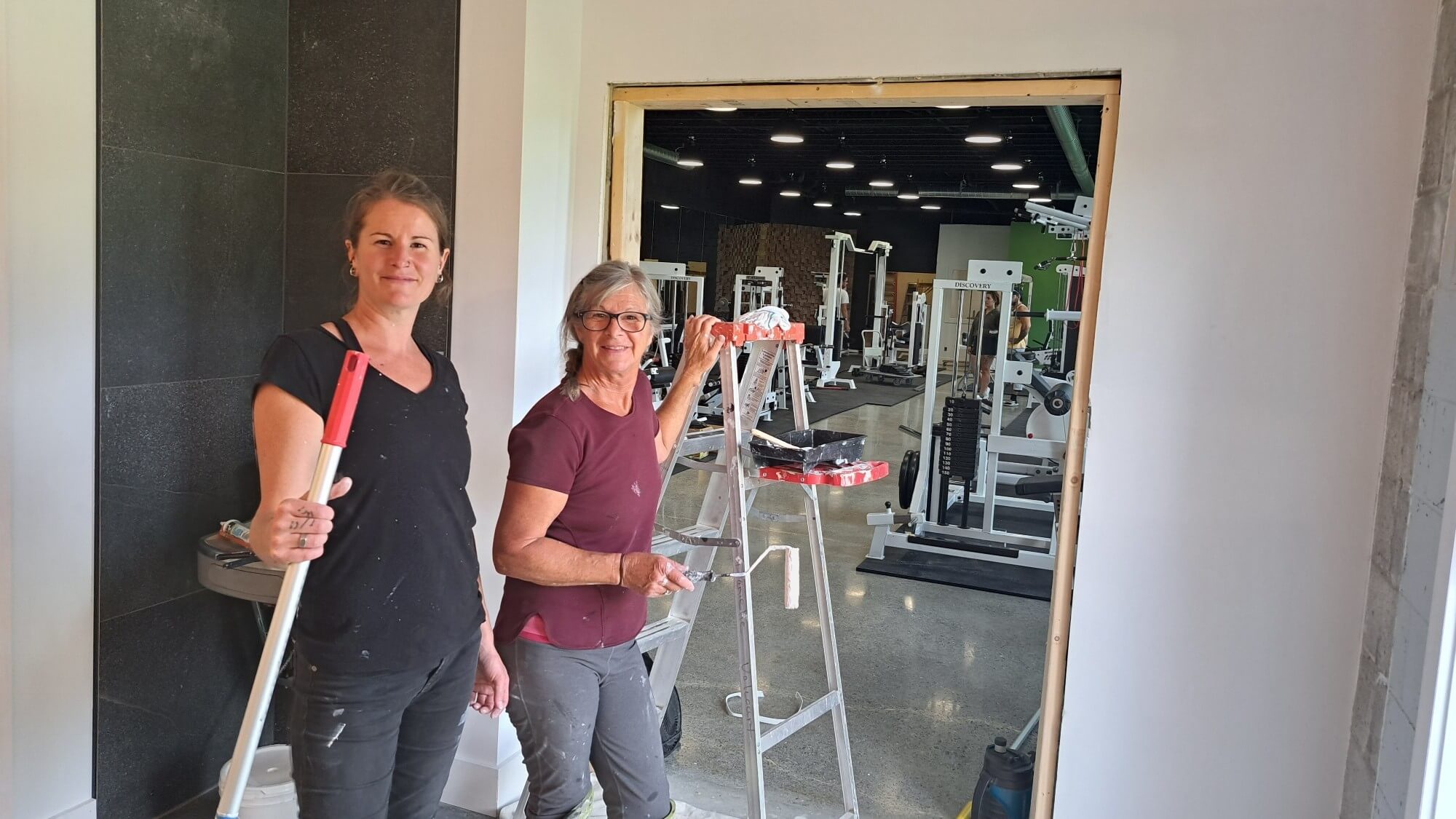 Deux femmes aux côtés d'un escabeau et devant l'entrée d'une salle d'entraînement.