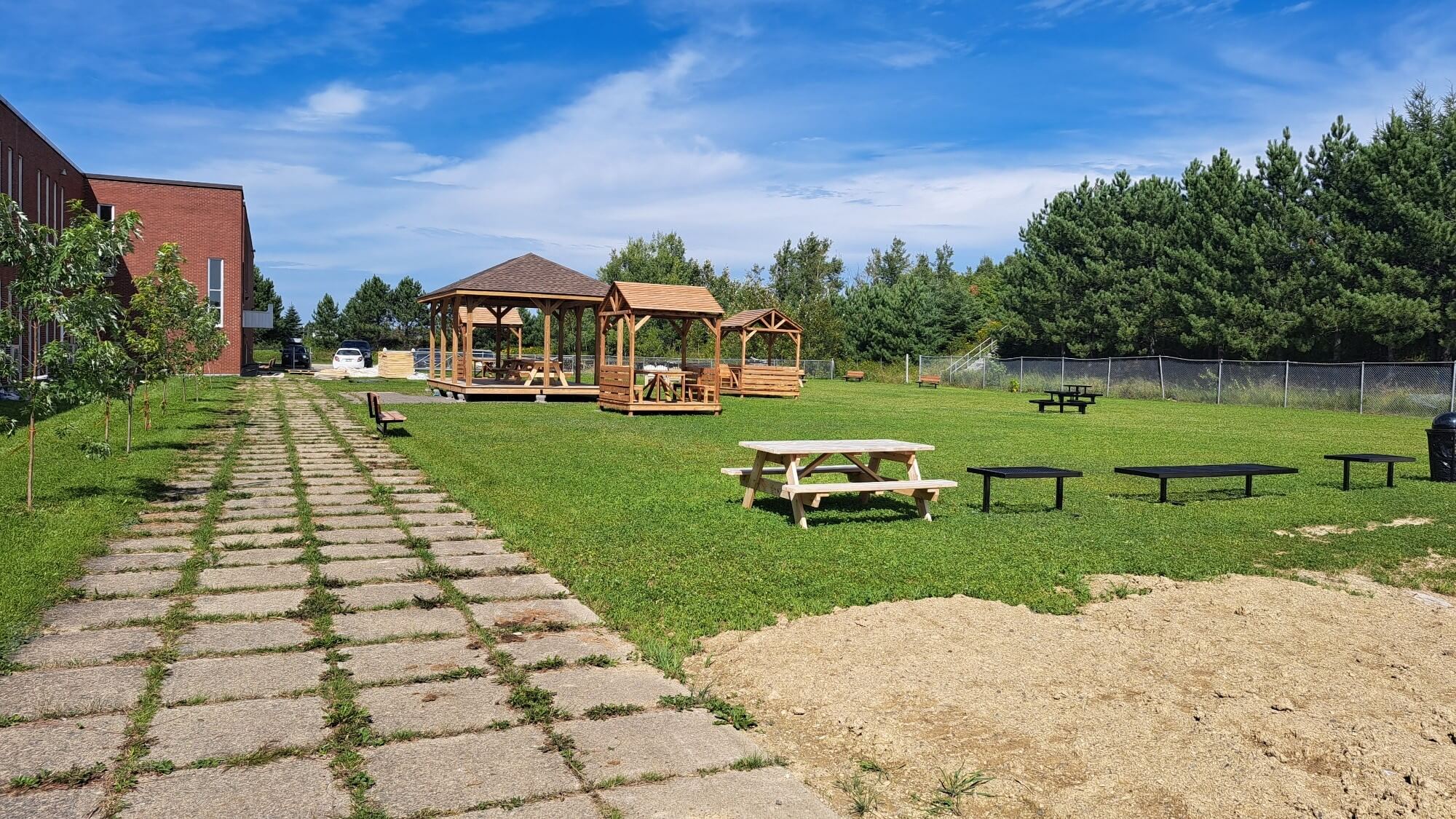 Gazebos, bancs et quelques autres infrastructures situé au côté d'un école sur une surface de pelouse verte.