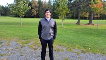 Homme habillé en noir gris debout devant un terrain de golf.