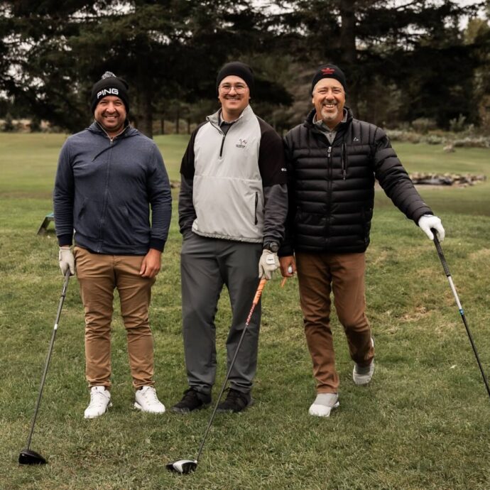 Trois hommes tenant leur bâton de golf sur un terrain de golf, lors d'une journée nuageuse et venteuse.
