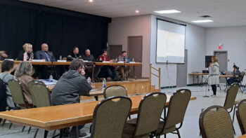 Une citoyenne est debout devant les membres d'un conseil municipale lors d'une réunion publique mensuelle.