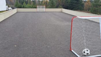 Une patinoire extérieur asphaltée comportant un ballon de soccer et deux filets de hockey.