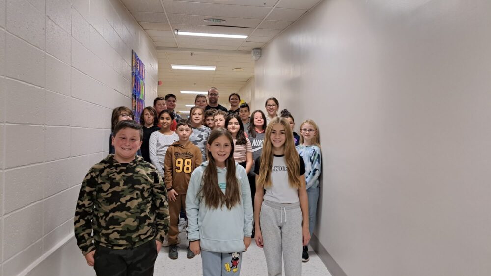 Des enfants de cinquième année pour une photo de groupe dans le corridor d'une école, les murs sont tous blanc.
