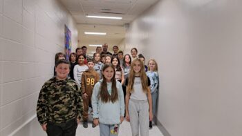 Des enfants de cinquième année pour une photo de groupe dans le corridor d'une école, les murs sont tous blanc.