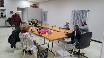 Sept personnes sont réunis autour d'une grande table, se réchauffement avec un café à la main dans une salle blanche à l'intérieur d'une caserne de pompier.