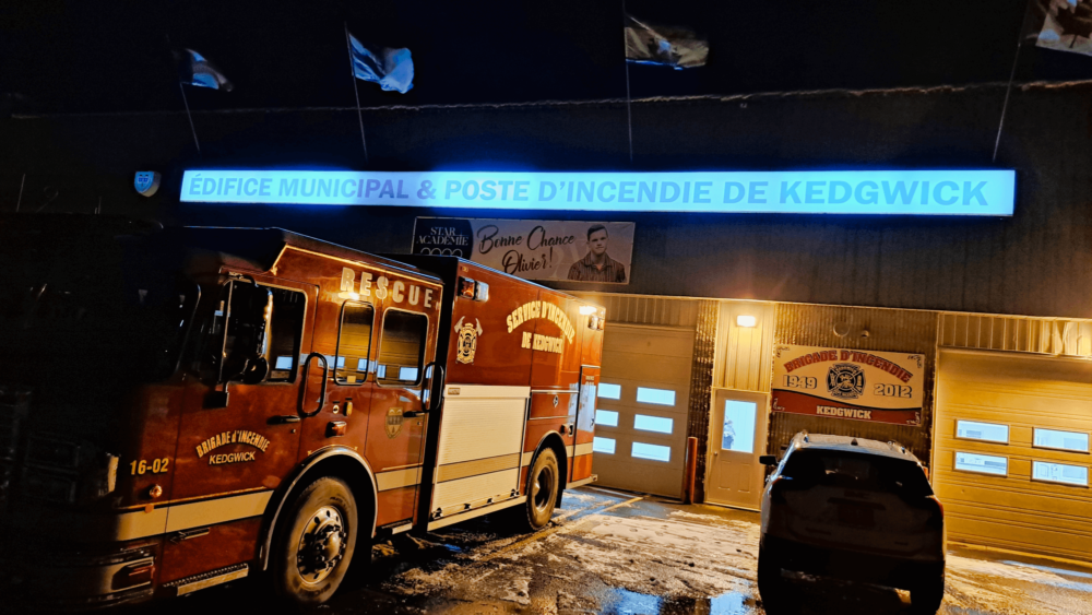 Camion de pompier situé devant une caserne en pleine en soirée et en plein noirceur.