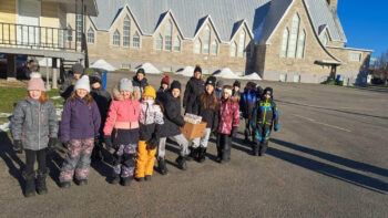 Une classe de quatrième année accompagnée de leur enseignante, tout habile manteau d'hiver, à l'extérieur lors d'une journée ensoleillée.