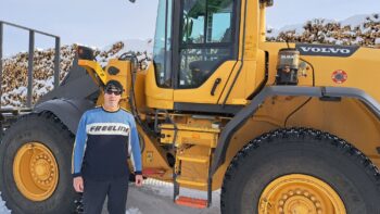 Homme vêtu de bleu devant une machinerie lourde jaune, en hiver.