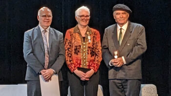 Trois personnes debout lors de la remise d'une médaille.