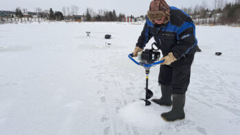 Homme creusant un trou sur un lac gelé afin de pratiquer la pêche sur la glace.