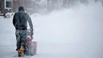 Un homme déneige sa cours avec sa souffleuse à neige.