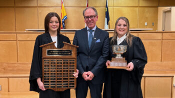 Deux étudiantes en droit tenant un trophée à la main avec au centre le professeur Jason Alcorn.