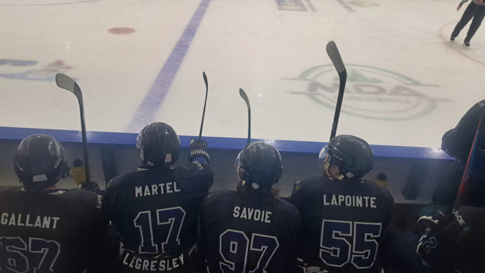 Des joueurs de hockey assis dans le banc des joueurs.