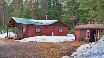 Chalet de couleur rouge entouré de conifères avec quelques butes de neige lors d'une journée de printemps.