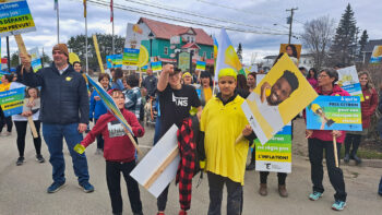 Des jeunes manifestants brandissant leur pancarte, à l'extérieure lors d'une journée de printemps grise et nuageuse.