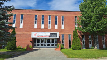 L'école Polyvalente Alexandre J. Savoie vue de face lors d'une journée ensoleillée d'été.