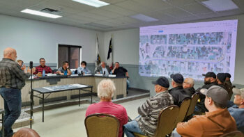 Un homme donne une conférence devant un groupe de citoyens, dans une salle de conseil municipal.