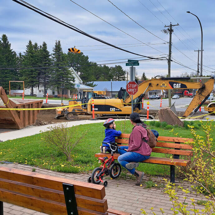 Une mère et son enfant sur un banc de parc, regardant les travaux extérieurs en cours, lors d'une journée pluvieuse.