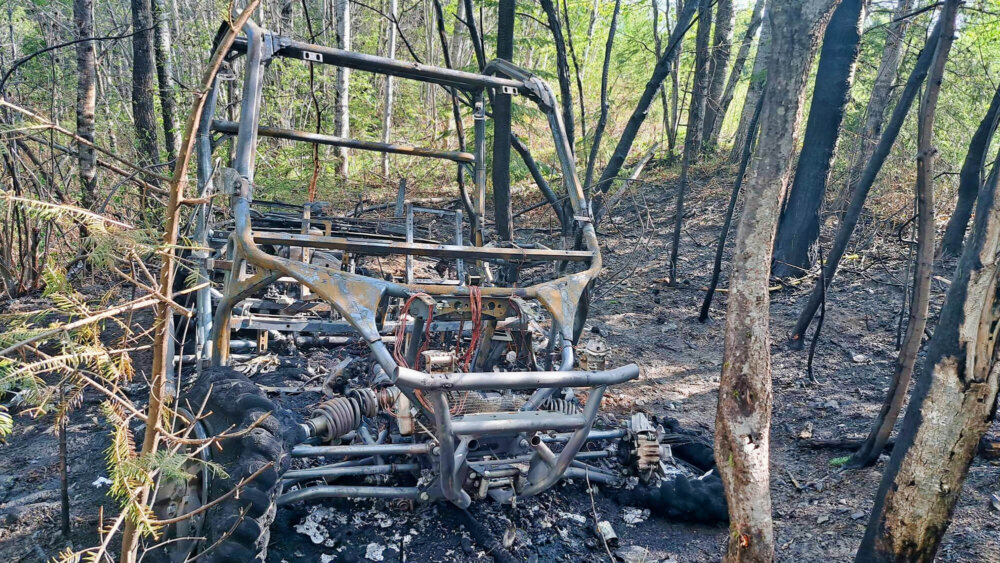 Véhicule de type côte-à-côte incendié en milieu boisé.